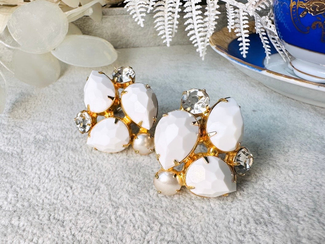 These vintage white earrings are an incredible pair of 1960s cluster earrings. Featuring opaque white faceted pear shaped stones, glass pearls and diamond rhinestones, these gold plated clip on earrings are fantastic. Each stone is prong set in a geometric pattern that mirrors each earring. A show-stopping rare pair of vintage earrings for a cocktail reception, award ceremony or wedding. Excellent vintage condition, please view all pics.