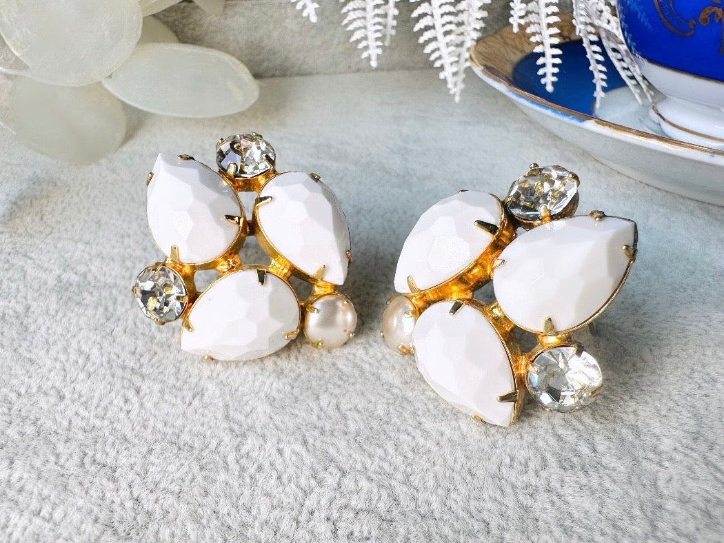 These vintage white earrings are an incredible pair of 1960s cluster earrings. Featuring opaque white faceted pear shaped stones, glass pearls and diamond rhinestones, these gold plated clip on earrings are fantastic. Each stone is prong set in a geometric pattern that mirrors each earring. A show-stopping rare pair of vintage earrings for a cocktail reception, award ceremony or wedding. Excellent vintage condition, please view all pics.