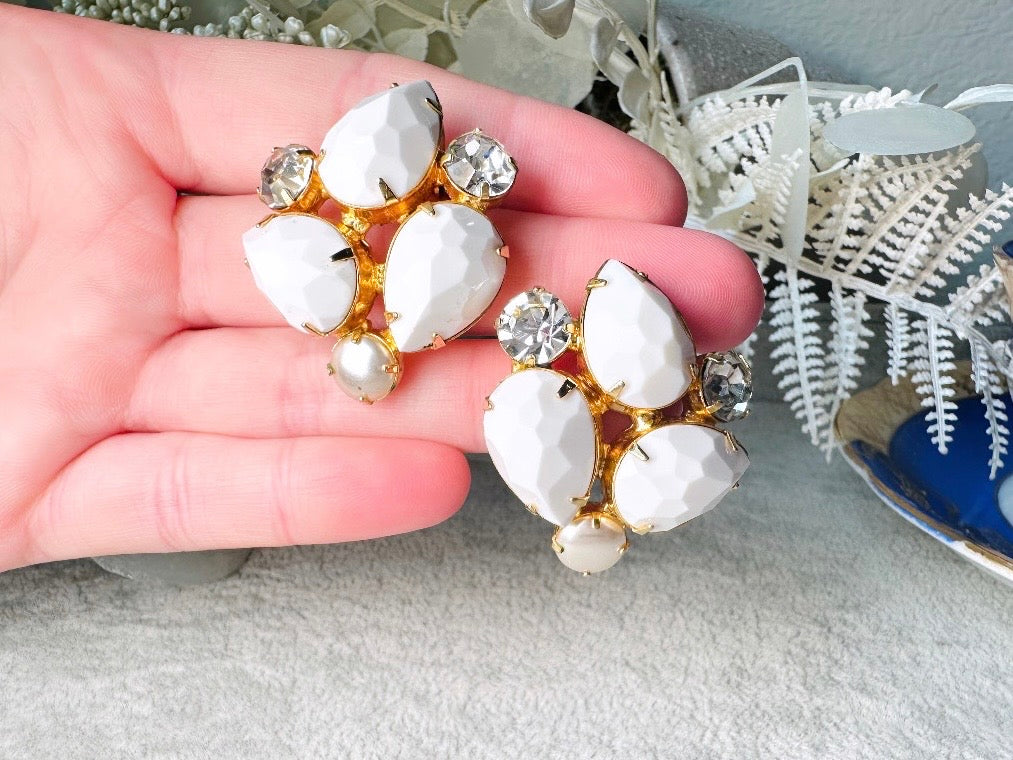 These vintage white earrings are an incredible pair of 1960s cluster earrings. Featuring opaque white faceted pear shaped stones, glass pearls and diamond rhinestones, these gold plated clip on earrings are fantastic. Each stone is prong set in a geometric pattern that mirrors each earring. A show-stopping rare pair of vintage earrings for a cocktail reception, award ceremony or wedding. Excellent vintage condition, please view all pics. held in hand