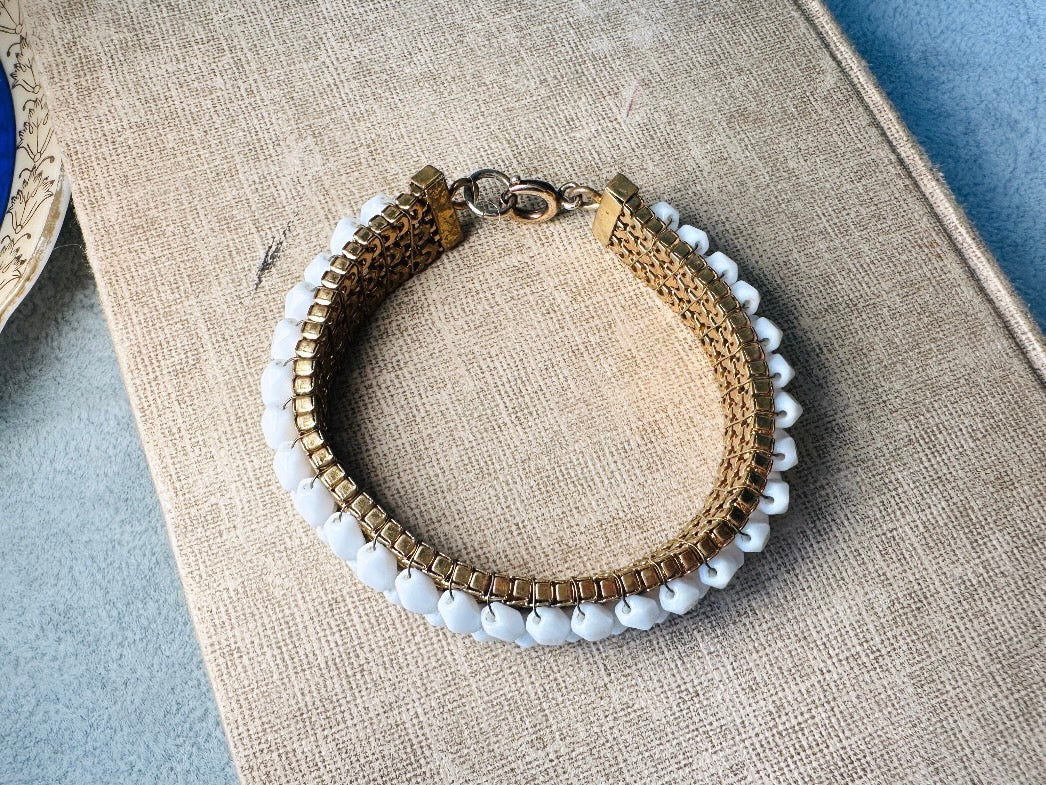 This beautiful white and gold 1960s vintage bracelet is so very pretty. Featuring triple strands of gold mesh chain with two strands of faceted milk glass crystals woven into the design. A simple spring ring closure brings this bracelet together. Easy to wear for everyday or would make a gorgeous bridal piece. A classic 1960s piece- in great vintage condition- &nbsp;please see all pics.

Dimensions: approximately 7.5" long, 0.5" wide.