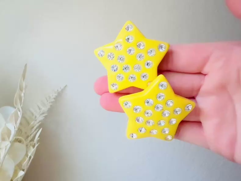 A pair of yellow star earrings from Piggle and Pop. A highly collectible pair of 1980s statement earrings. These yellow star earrings are bright banana yellow opaque lucite with diamond rhinestone accents. Huge vintage star clip ons with major rockstar vibes. Video