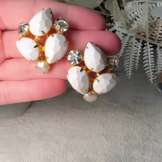 These vintage white earrings are an incredible pair of 1960s cluster earrings. Featuring opaque white faceted pear shaped stones, glass pearls and diamond rhinestones, these gold plated clip on earrings are fantastic. Each stone is prong set in a geometric pattern that mirrors each earring. A show-stopping rare pair of vintage earrings for a cocktail reception, award ceremony or wedding. Excellent vintage condition, please view all pics. video