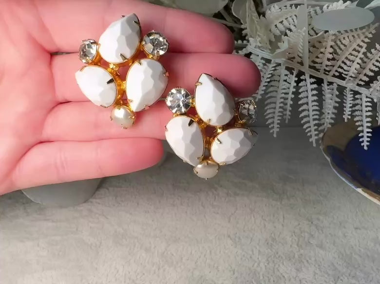 These vintage white earrings are an incredible pair of 1960s cluster earrings. Featuring opaque white faceted pear shaped stones, glass pearls and diamond rhinestones, these gold plated clip on earrings are fantastic. Each stone is prong set in a geometric pattern that mirrors each earring. A show-stopping rare pair of vintage earrings for a cocktail reception, award ceremony or wedding. Excellent vintage condition, please view all pics. video