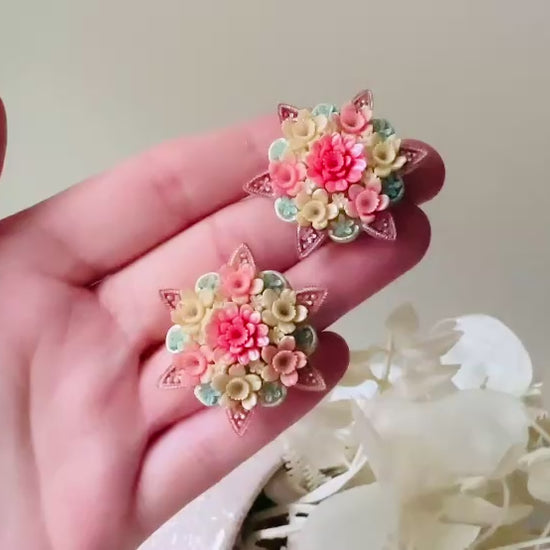 Video of vintage 1950s Japanese floral celluloid earrings are so colorful. Carved celluloid bursting with sakura blossoms and flowers, these earrings are on the larger side and are painted with a beautiful pearlized pink, blue and light cream. The star-shaped base and raised beaded edges are also characteristic of vintage Japanese celluloid jewelry. They are 1.5" in size.