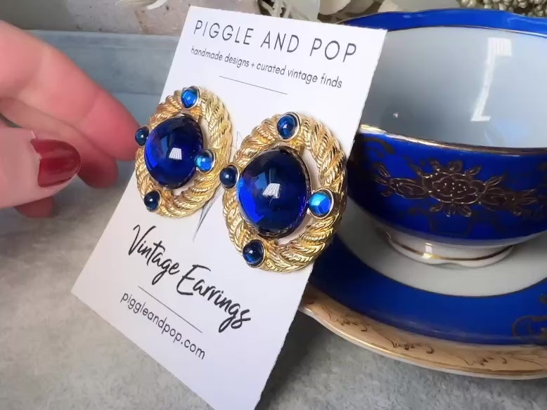 These vintage Park Lane gold rope earrings with cobalt blue cabochons are absolutely out of this world! Vibrant deep blue cabochons glow as they are surrounded by an intricate gold rope border that is accented with four more smaller blue jewels. These stones are so vibrant and vividly pop against their gold setting. Ultimate 80s mega star vibes, post style for pierced ears. Highly collectible signed designer pair in excellent vintage condition, no major flaws to note. video