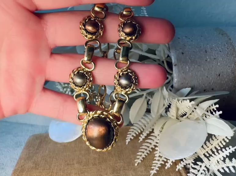 This vintage Etruscan style Liz Claiborne gold chain necklace is a beautifully unique find. Featuring large curb chain links with round cabochons of faux hematite and bronze set in gold bezels. In the center is a larger bronzed oval cabochon in the same style of gold roped bezel. Signed on back of center cabochon as well as the signature LCI triangle hang tag on the end of extender chain. Versatile while making a statement, and incredibly flattering. Minimal wear from age, no major flaws to note.