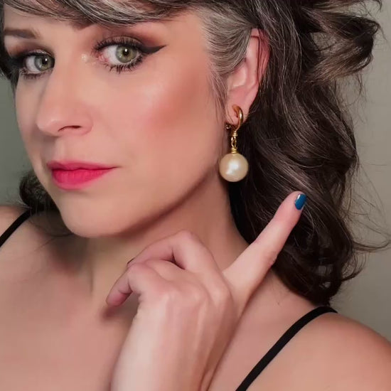 These vintage matte gold and cream pearl drop earrings are clip ons, shown on a model. They are very elegant. They give the appearance of half huggie hoops in a beautiful satin matte finish gold, with a striking oversized cream glass pearl. These Etruscan statement drop earrings are very on trend. These earrings are 2 inches long, unsigned in excellent condition. Video