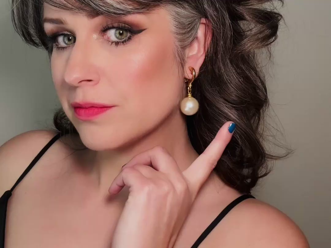 These vintage matte gold and cream pearl drop earrings are clip ons, shown on a model. They are very elegant. They give the appearance of half huggie hoops in a beautiful satin matte finish gold, with a striking oversized cream glass pearl. These Etruscan statement drop earrings are very on trend. These earrings are 2 inches long, unsigned in excellent condition. Video