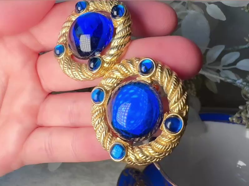 These vintage Park Lane gold rope earrings with cobalt blue cabochons are absolutely out of this world! Vibrant deep blue cabochons glow as they are surrounded by an intricate gold rope border that is accented with four more smaller blue jewels. These stones are so vibrant and vividly pop against their gold setting. Ultimate 80s mega star vibes, post style for pierced ears. Highly collectible signed designer pair in excellent vintage condition, no major flaws to note. video of details.
